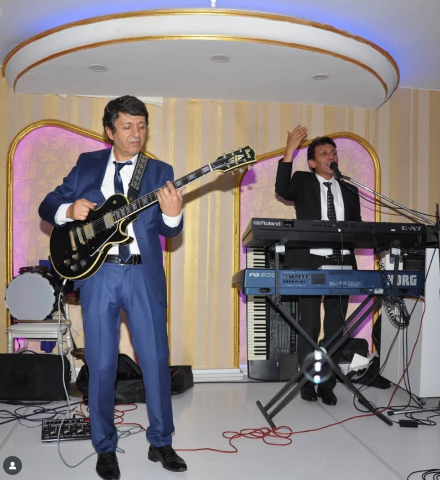 Sahnede siyah Ibanez elektro gitarıyla performans sergileyen Bayram Telli ve sahne arkadaşı klavye başında